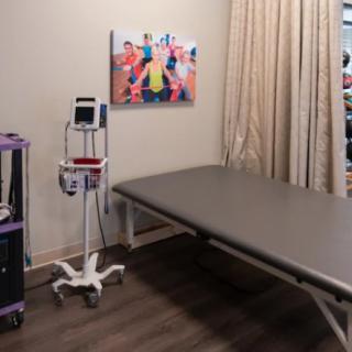 A medical clinic room featuring a treatment table, medical equipment, and artwork on the wall.