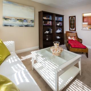 A cozy living room with modern furniture, including a white coffee table, a bookshelf filled with books, and an armchair adorned with a red throw.