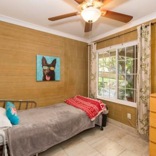 A cozy bedroom with a single bed, featuring a dog painting and a ceiling fan.