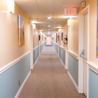 A long, carpeted hallway with doors on both sides and overhead lighting.
