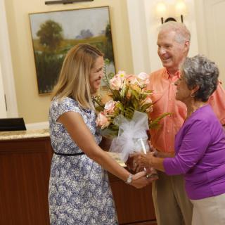 A woman hands a bouquet of flowers to an elderly couple in a reception area.