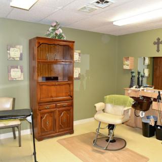 A cozy beauty salon featuring a comfortable barber chair, wooden shelves, and soft green walls.