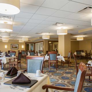 An elegantly furnished dining area with neatly arranged tables and chairs, softly lit by overhead lights.