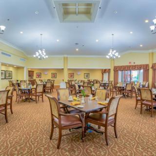 A spacious and well-lit dining room with neatly arranged tables and chairs, featuring elegant chandeliers.