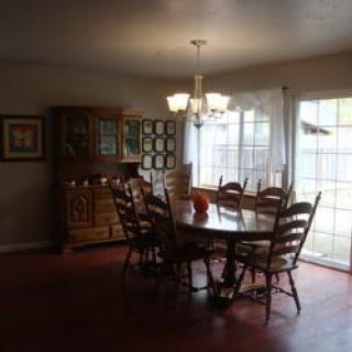 A cozy dining room with a wooden table and chairs illuminated by natural light from large windows.