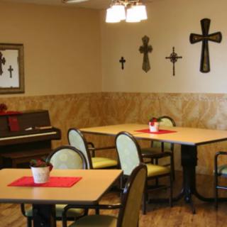 A cozy dining room with tables, chairs, a piano, and decorative crosses on the wall.
