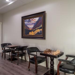 A cozy interior with a chess set on a table, surrounded by chairs and adorned with a colorful painting on the wall.