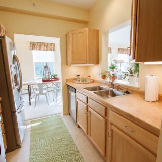 A cozy kitchen with wooden cabinets and a view into the dining area, illuminated by natural light.