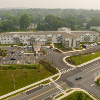 Aerial view of a large building with adjacent parking lot and surrounding roads in an urban area.