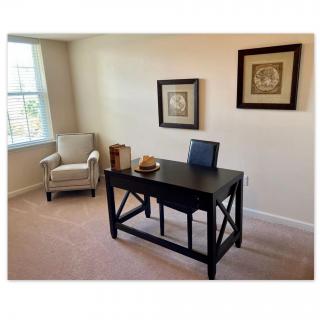 A minimalist home office with a dark wood desk, an armchair, and framed artwork on the wall.