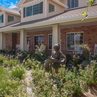 A building with a brick exterior surrounded by lush landscaping and garden statues.