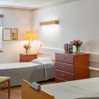 A tidy hospital room with two single beds, wooden furniture, and decorative flowers.