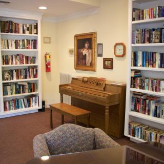 A cozy library corner featuring bookshelves filled with books, a piano, and comfortable seating.