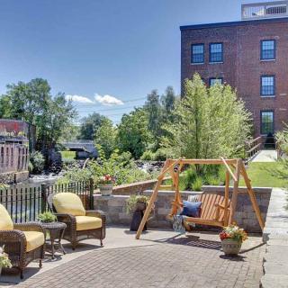 A sunny outdoor patio with comfortable seating and a wooden swing, set against a backdrop of greenery and a brick building.