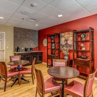 A cozy indoor lounge area with tables and chairs, featuring a red accent wall and decorative bookshelves.