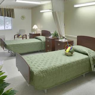 A clean and organized hospital room with two patient beds, each featuring green bedding and separated by a curtain.