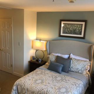 A cozy bedroom with a decorated bed, bedside lamp, and framed artwork on the wall.