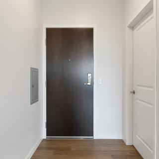 A simple hallway with a wooden door, white walls, and wood flooring.
