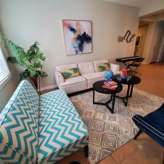 A cozy living room with modern decor, featuring a sofa, a patterned chair, coffee tables, and artwork on the wall.