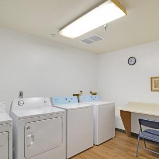 A clean and organized laundry room with washing machines, a dryer, and a small table with a chair.