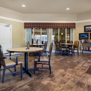 A cozy dining area with wooden floors, round tables, and chairs, complemented by a small library section.