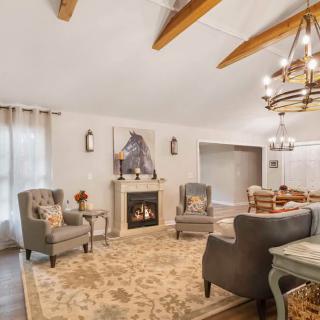 A cozy living room featuring a fireplace, elegant armchairs, and a chandelier under a beamed ceiling.