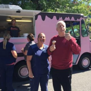 A group of people enjoying ice cream outside a pink ice cream truck on a sunny day.