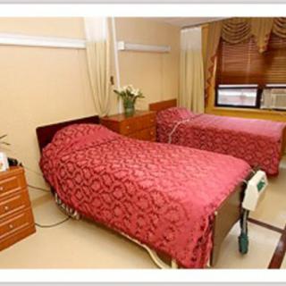 A hospital room featuring two neatly made patient beds with red bedspreads.