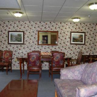 A cozy waiting room with patterned wallpaper, featuring chairs, a sofa, and framed artwork.