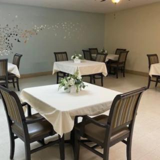 A dining room with tables set for guests, featuring floral centerpieces and neatly arranged tablecloths.
