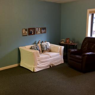 A cozy living room with a white sofa and dark armchair against a blue wall.