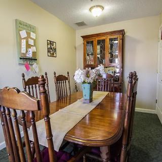 A cozy dining room with a wooden table and chairs, decorated with a vase of flowers and a table runner.