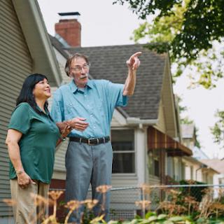 An elderly couple enjoying a moment together in their garden, sharing a smile and pointing at something interesting.