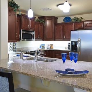 A modern kitchen with cherry wood cabinets, stainless steel appliances, and a granite countertop adorned with blue glassware.