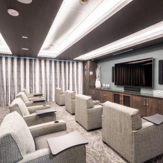 A luxurious home theater room featuring comfortable recliner seating and a large television screen, designed with modern aesthetics.