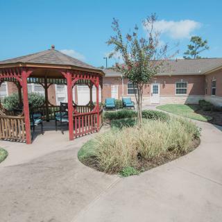 A serene outdoor space featuring a red gazebo, surrounded by landscaped gardens and a pathway.