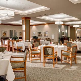 An elegant restaurant dining room with neatly arranged tables and chairs, featuring warm lighting and tasteful decor.