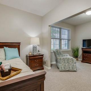 A cozy bedroom with a bed, lamp, armchair, and TV.