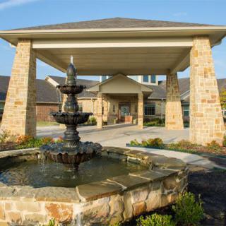 A building entrance featuring a stone fountain and landscaped surroundings.