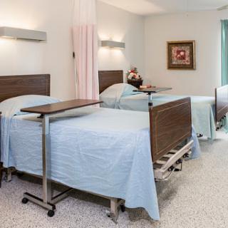 A view of a patient room in a hospital featuring multiple beds with blue linens and bedside tables.