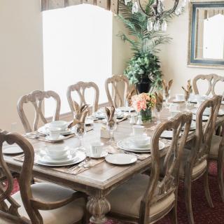 An elegantly set dining table with neatly arranged dishes and silverware, surrounded by chairs in a tastefully decorated room.