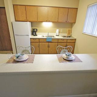 A compact kitchen with a breakfast counter set for two, featuring wooden cabinets and a window providing natural light.