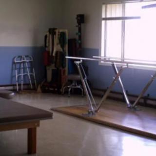 An empty physical therapy room equipped with parallel bars and a walker.