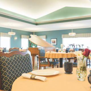 A bright dining room with neatly arranged tables, chairs, and a decorative piano.