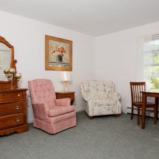 A cozy living room with vintage furniture, including an armchair, a dresser, and a dining table set.