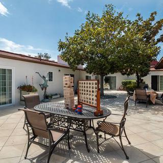 A sunny patio with outdoor furniture and a large Connect Four game under a tree.