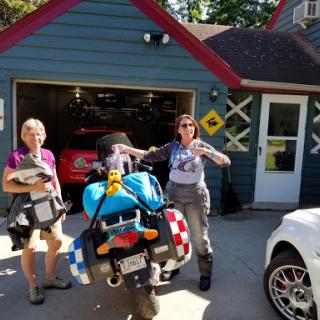 Two women preparing for a journey with their motorcycle, surrounded by a home garage setting.