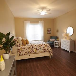 A cozy bedroom with warm lighting, featuring a floral bedspread, wooden flooring, and elegant decor.