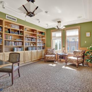A cozy library reading room with bookshelves, comfortable chairs, and natural light streaming through the windows.