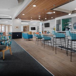A modern, spacious lobby featuring a bar area with teal seating and wooden accents.